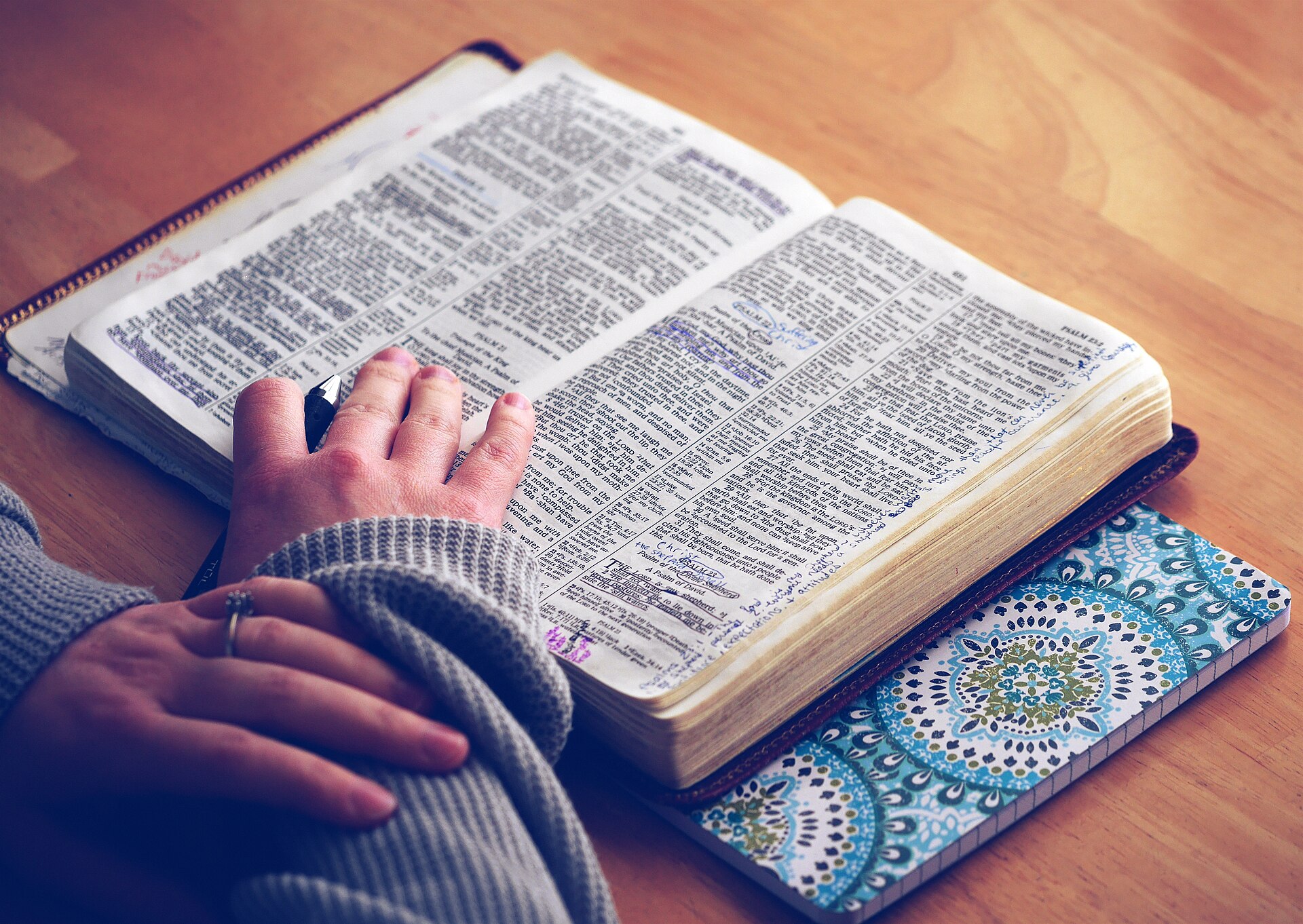 A hand resting on an open Bible with handwritten notes in the margins